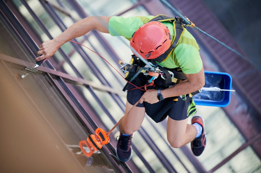 Industrial mountaineering worker cleaning window outside building.